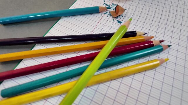 A close view of classroom materials on squared exercise books includes a small globe, colored pencils, yellow glue stick, white eraser, scissors and turquoise cloth.