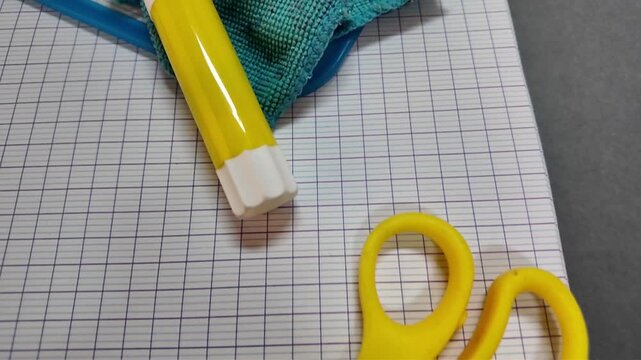 A close view of classroom materials on squared exercise books includes a small globe, colored pencils, yellow glue stick, white eraser, scissors and turquoise cloth.