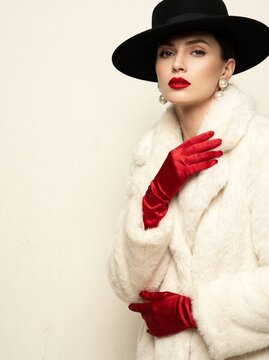 Fashionable Woman Wearing a White Faux Fur Coat and Black Hat with Red Gloves and Lipstick Elegant Vintage Style Portrait