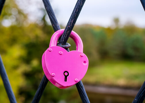 Pink heart padlock attached to metal railing as a wedding tradition, symbolizing love, fidelity, commitment and lasting marriage.