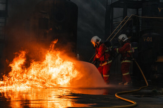 Firefighter rescue worker confronts fire during disasters and accidents, spraying foam across industrial blaze while protective gear shields team from intense heat and danger