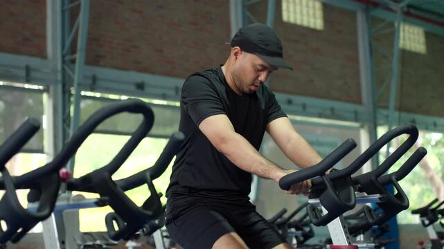 Man exercising on a stationary bike at an indoor fitness center, improving cardiovascular health, building muscle endurance and supporting healthy aging and longevity.