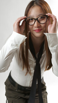 Smiling Young Asian Woman Adjusting Black Eyeglasses in White Shirt and Tie