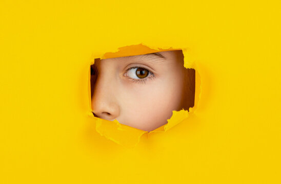 Human eye closeup. Child's eye looking throughs hole. Boy breaks paper. Boy peeks through a cut hole in red paper wall