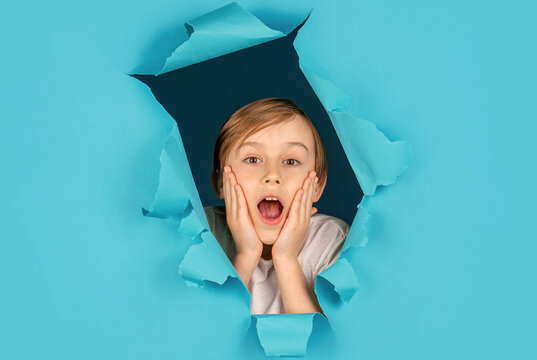 Breaking paper background. Kid looks through hole. Blonde boy looks through ripped paper