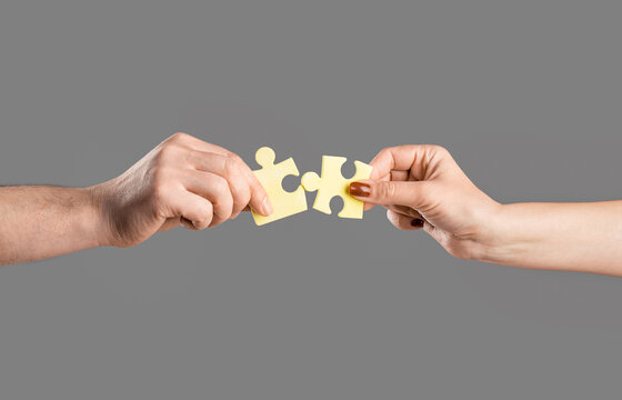 Teamwork concept. Closeup hand of connecting jigsaw puzzle. Two hands trying to connect couple puzzle piece on gray background
