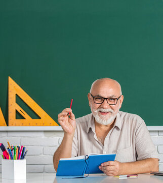 School male teacher reads book. Male teacher with laptop in class sits at the table