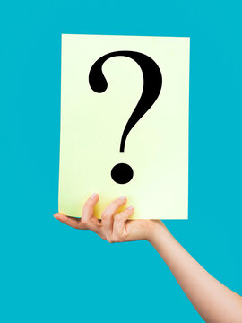Question mark symbol. Space for text. Hand holding paper a question mark. Female hand holding question mark, query, why or what. Hand holding a white question mark paper against a blue background