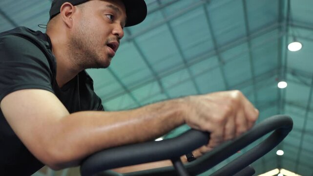 Close-up man exercising on a stationary bike at an indoor fitness center, improving cardiovascular health, building muscle endurance and supporting healthy aging and longevity.