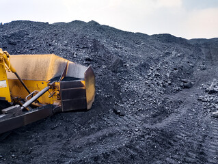 Heavy bulldozer machine working at an open pit coal mining site clearing black minerals and coal piles. © Badli jr