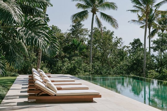 Infinity pool at a tropical modernism resort villa with teak sun loungers and lush greenery under bright midday light