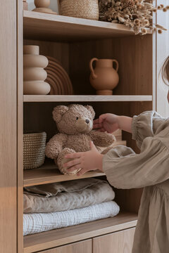 Woman arranging teddy bear among ceramics and folded blankets in wooden shelving unit
