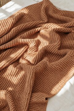 Closeup of warm brown knitted throw with soft folds in sunlit bedroom setting