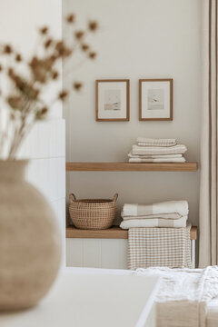 Blurred ceramic vase framing folded linens and oak shelving in a calm neutral interior