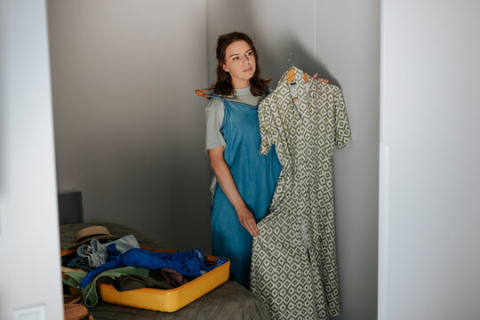 Woman chooses dress while packing yellow suitcase for travel