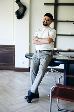 Man with arms crossed leaning on a black desk, smiling at the camera, embodying success and professionalism in a contemporary workspace