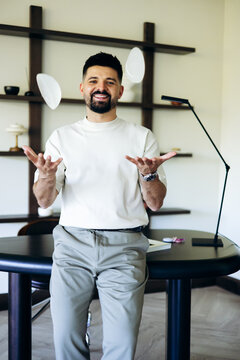 Smiling man juggling white plates in a modern office, representing professional workload management and career challenges