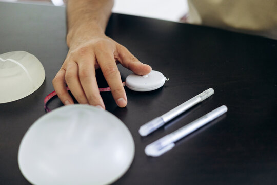 Professional hand holding measuring tape near breast implants and surgical markers, preparing for plastic surgery consultation