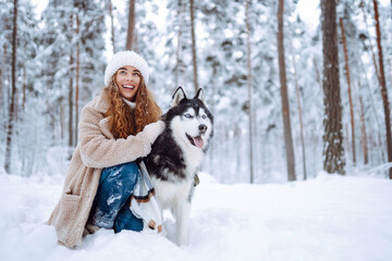 Young woman is having fun in snow-covered forest with Siberian husky. Woman and her dog are out for a walk on winter day, enjoying their time together. Concept of pets, fun, and leisure. © maxbelchenko