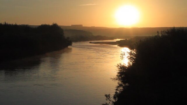 RAW and unedited stock footage capturing a beautiful golden sunrise over the historic Tigris River (Dicle River), with light morning mist rising from the water surface. Authentic, unprocessed landscap