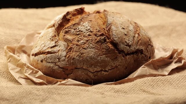A round, rustic sourdough loaf with a crispy, crackled crust, dusted with flour and resting on crumpled brown wrapping paper in vintage style