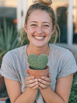 Cheerful Blonde Woman Showing Heart Shaped Succulent Cactus in Terracotta Pot