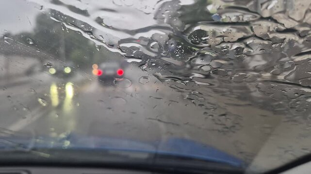 Rain drops splattering across automobile windshield during a wet urban drive. Interior dashboard perspective shot.