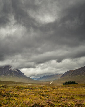 Dark rain clouds hang over the heather moorlands and A82 road passing through Glencoe in the Highlands of Scotland