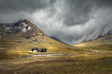 The River Coupall passes by the Wee White House at Glencoe in the Highlands of Scotland with Buachaille Etive Mor shrouded in dark rain clouds behind © Jon Ingall