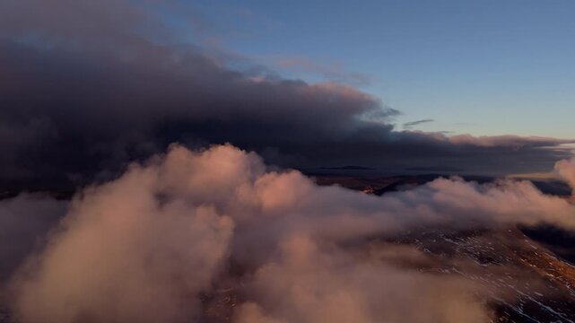 Aerial drone shot of majestic clouds rolling over mountain peaks at sunset