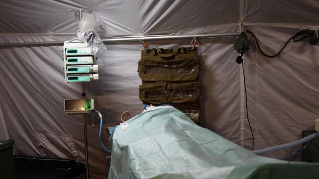 Military field hospital interior with an emergency treatment bed infusion pumps and breathing equipment prepared for intensive care and lifesaving medical procedures in a temporary tent