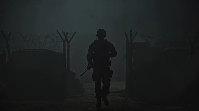 Soldier silhouette walking in fog near border fence for military patrol, dark cinematic defense concept