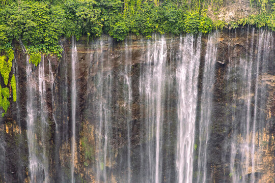 Tumpak Sewu Waterfall in Lumajang, East Java, Indonesia. Hundreds of cascading streams fall from a curved cliff into a lush tropical gorge, surrounded by dense rainforest and rising mist.