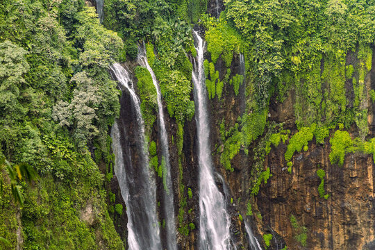 Tumpak Sewu Waterfall in Lumajang, East Java, Indonesia. Hundreds of cascading streams fall from a curved cliff into a lush tropical gorge, surrounded by dense rainforest and rising mist.