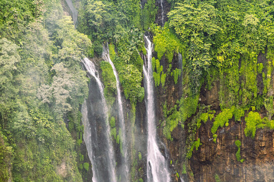 Tumpak Sewu Waterfall in Lumajang, East Java, Indonesia. Hundreds of cascading streams fall from a curved cliff into a lush tropical gorge, surrounded by dense rainforest and rising mist.