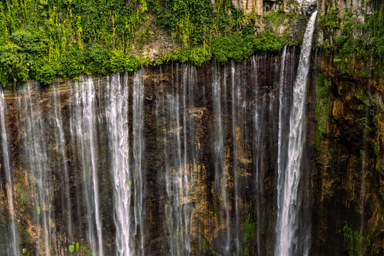 Tumpak Sewu Waterfall in Lumajang, East Java, Indonesia. Hundreds of cascading streams fall from a curved cliff into a lush tropical gorge, surrounded by dense rainforest and rising mist.