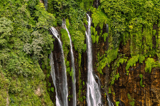 Tumpak Sewu Waterfall in Lumajang, East Java, Indonesia. Hundreds of cascading streams fall from a curved cliff into a lush tropical gorge, surrounded by dense rainforest and rising mist.