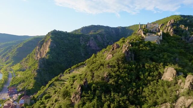 Aerial view of Aggstein Castle ruins perched on a rocky mountain ridge surrounded by dense green forest and dramatic valleys in the Wachau Valley of Austria under clear daylight