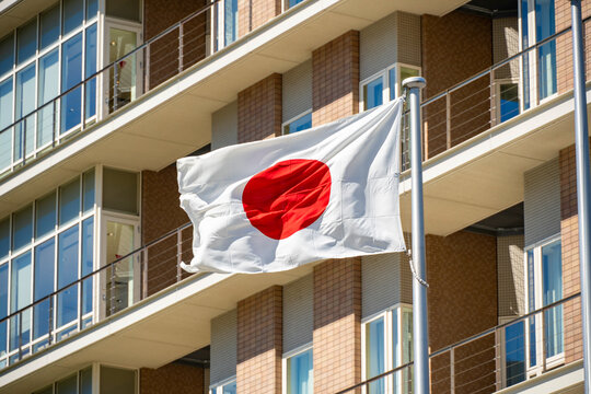 Japanese national flag waving in the wind with a modern building in the background