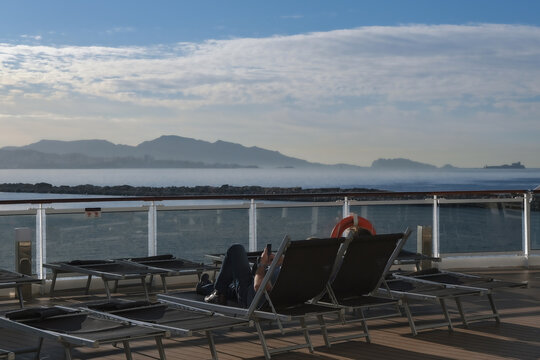 Pooldeck or swimmingpool with sun deck on modern cruiseship cruise ship liner in port with sun loungers ready for cruising to Mediterranean on sunny day with city skyline in background