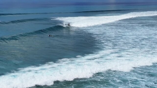 Aerial view of a lone surfer riding a breaking wave in the deep blue ocean with white foam patterns in Thulusdhoo, Kaafu Atoll, Maldives.