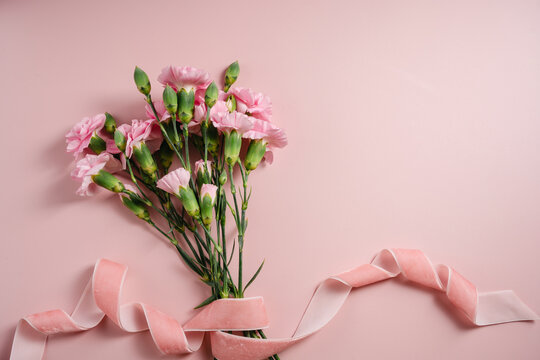 Pink carnations tied with velvet ribbon on pastel pink background with copy space