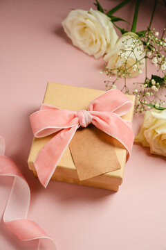 Gift box with white ribbon and cream roses on pastel pink background