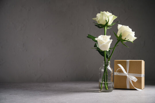 Kraft gift box with white satin ribbon and cream roses on textured background