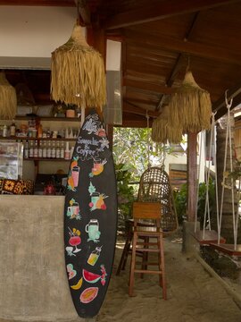 Beach cafe with surfboard chalkboard menu, raffia lamps, rattan hanging chair and rope swing on sand floor