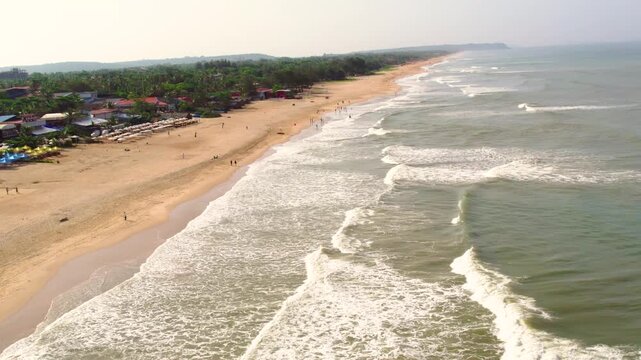 Aerial view of Vagator Beach with golden sands, gentle waves, and lush coastal vegetation along the shoreline in Anjuna, Goa, India.