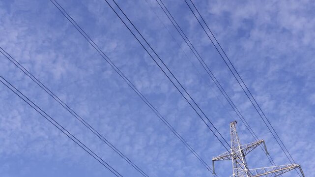 Tall lattice steel pylon supports multiple power lines against a pale blue sky with wispy cirrus clouds