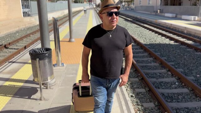 Hombre caminando por el and&eacute;n con su maleta mientras espera el tren
