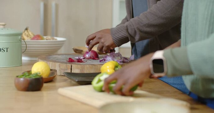 Right hand placing halved green pepper and slicing while left hand peeling red onion for salad