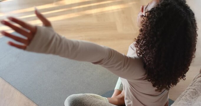 Yogi is extending arm, lifting overhead, bringing palms together on mat in sunlit room to center